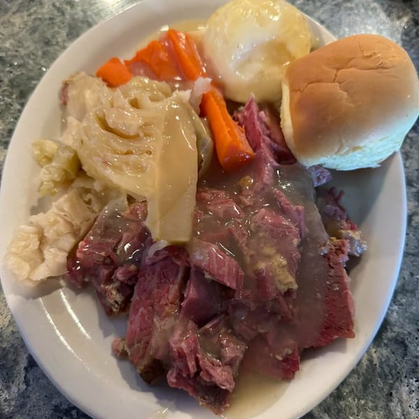Corned beef and cabbage with carrots, potatoes, and a dinner roll on a white plate.