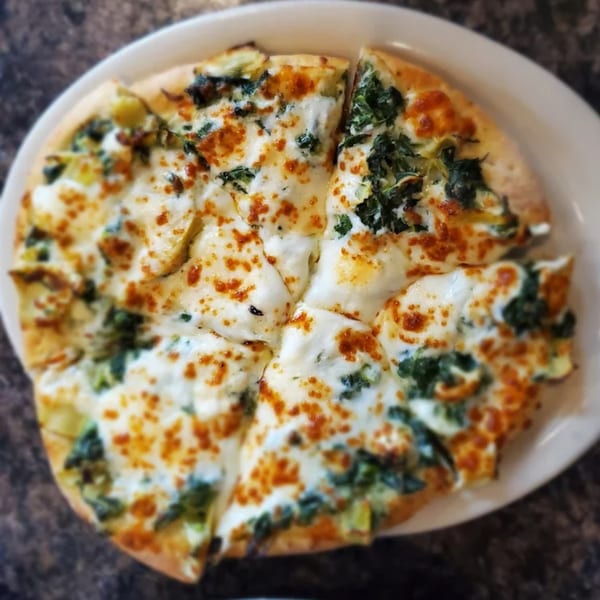A white pizza from Piazzano's, topped with melted cheese and spinach, cut into slices.