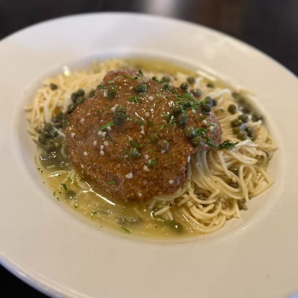 Piazzano's Chicken Piccata with capers and parsley over spaghetti in a white bowl.