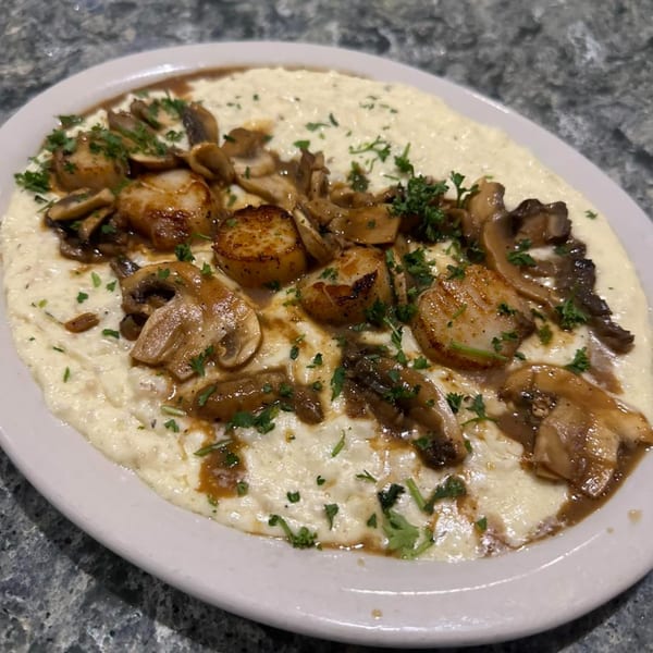 Seared scallops and mushrooms in a rich brown sauce, served over creamy white polenta, garnished with parsley.